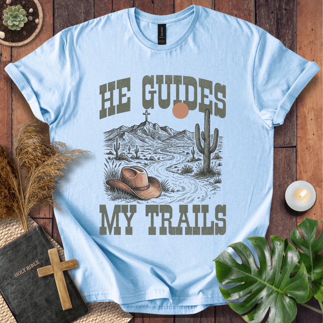 A Christian t-shirt with a desert landscape, cowboy hat, and cross, reading He Guides My Trails.