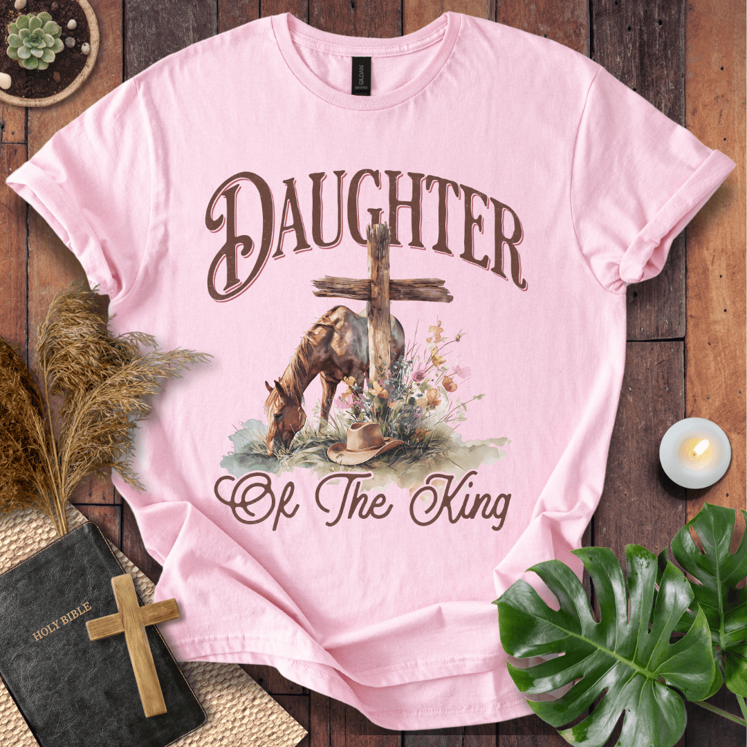 t-shirt with "Daughter of the King" text, a grazing horse, wooden cross, cowboy hat, and wildflowers.