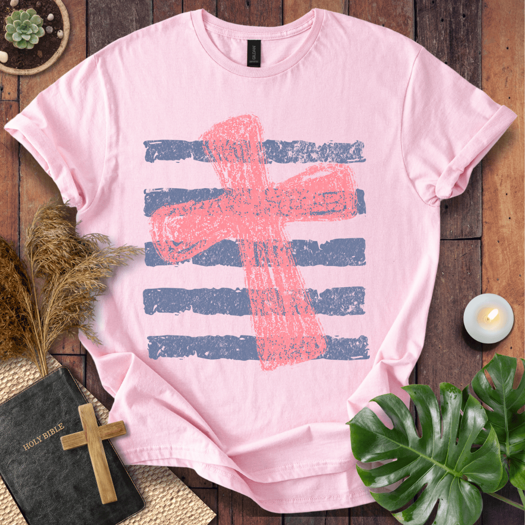 Distressed pink cross over blue horizontal stripes on a t-shirt, styled with a Bible and wooden cross.