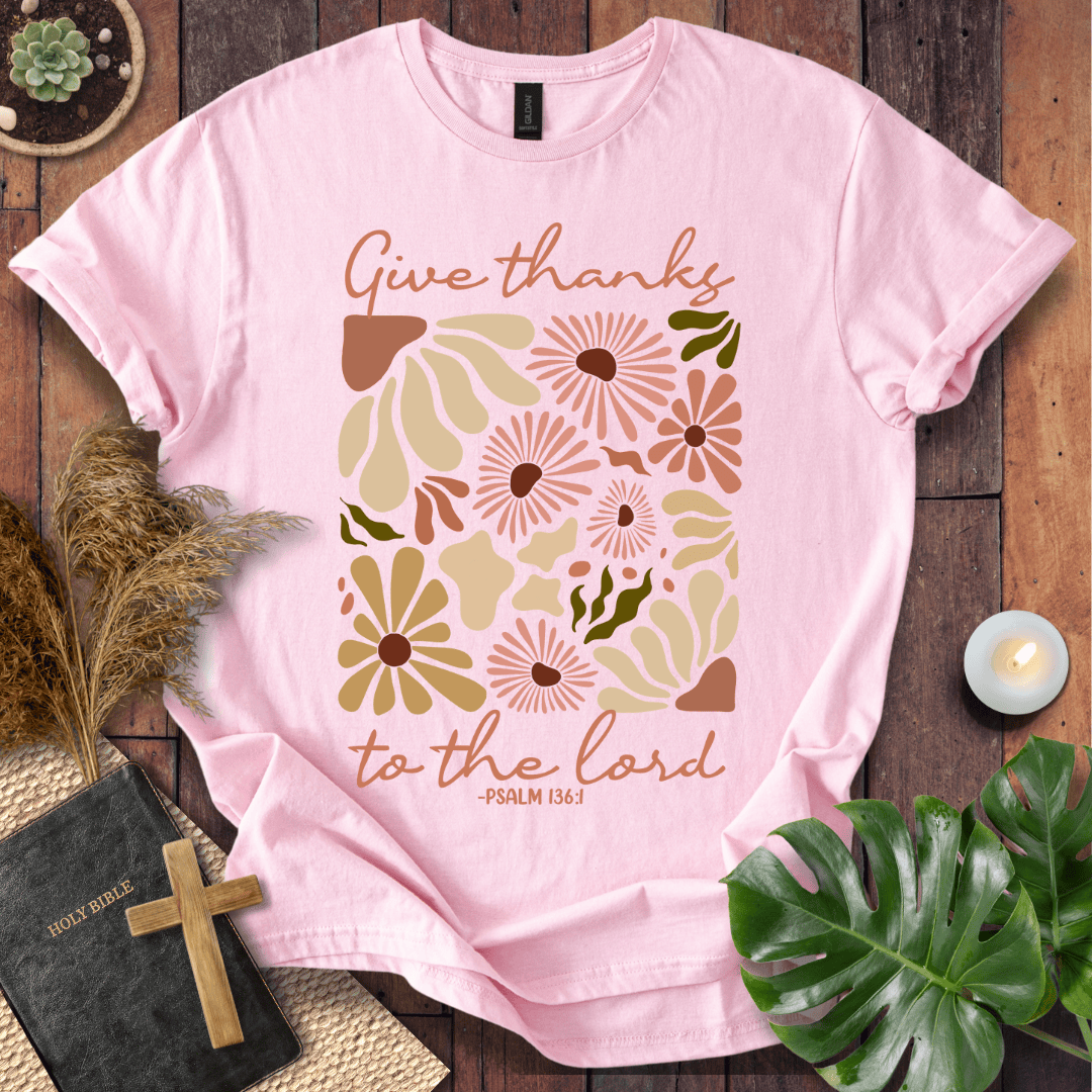 Give Thanks to the Lord Psalm 136:1 white graphic t-shirt with retro boho rust and sage wildflowers on a wood background.
