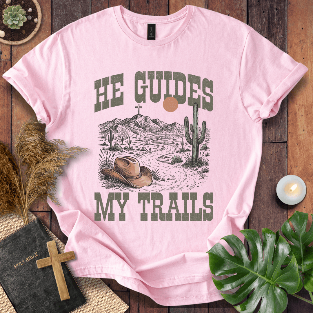 A Christian t-shirt with a desert landscape, cowboy hat, and cross, reading He Guides My Trails.