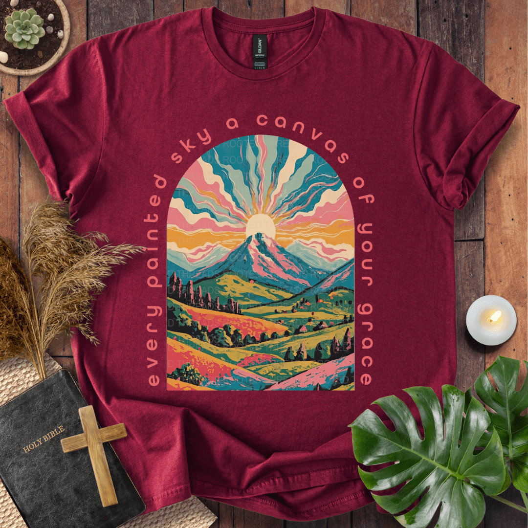 “Every painted sky a canvas of Your grace” Christian t-shirt—arched mountain sunrise with rays, rolling hills, floral accents.