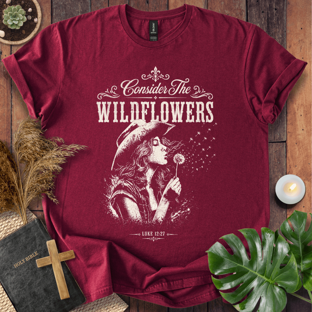 graphic tee reading Consider the Wildflowers Luke 12:27, featuring a woman in a cowboy hat blowing a dandelion.