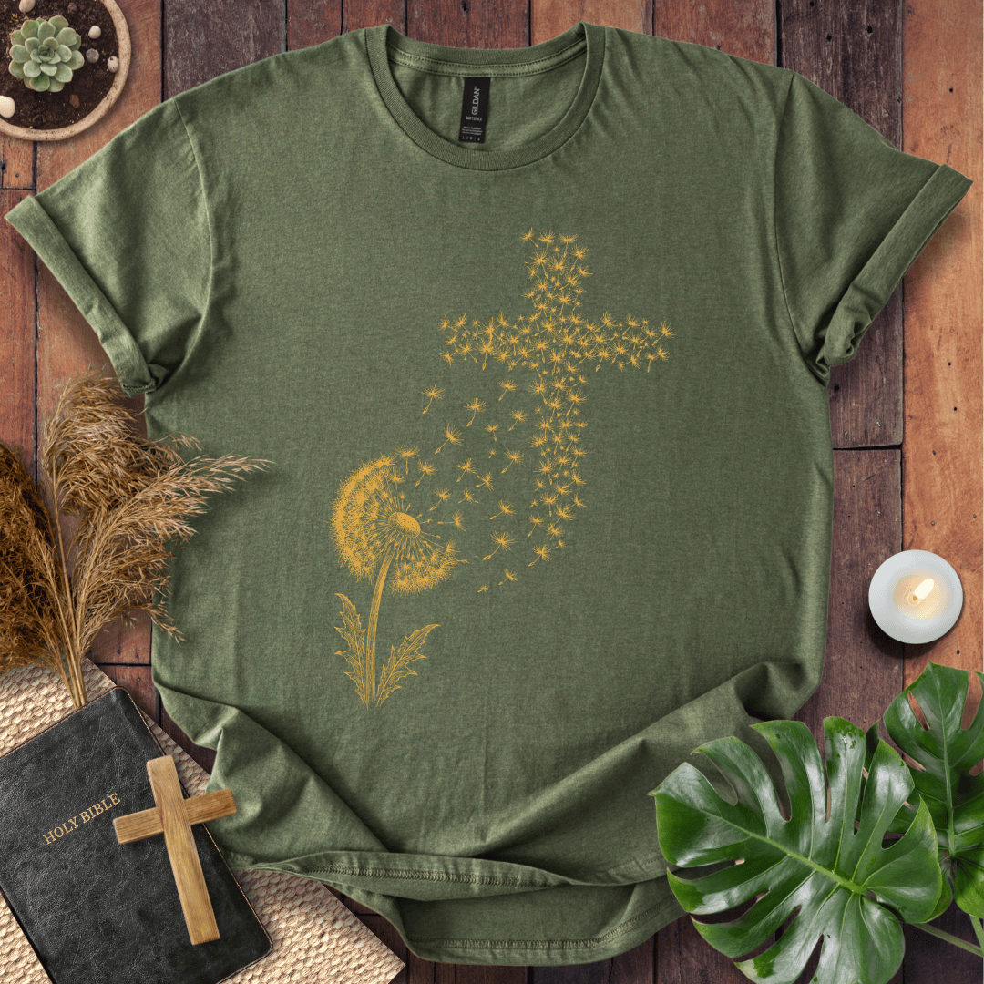 graphic t-shirt featuring a golden dandelion with seeds blowing in the wind to form a Christian cross shape.