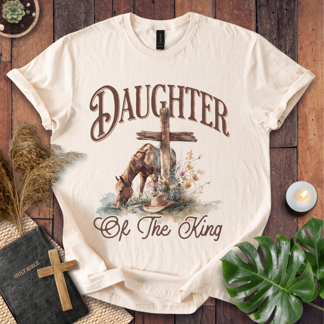 t-shirt with "Daughter of the King" text, a grazing horse, wooden cross, cowboy hat, and wildflowers.