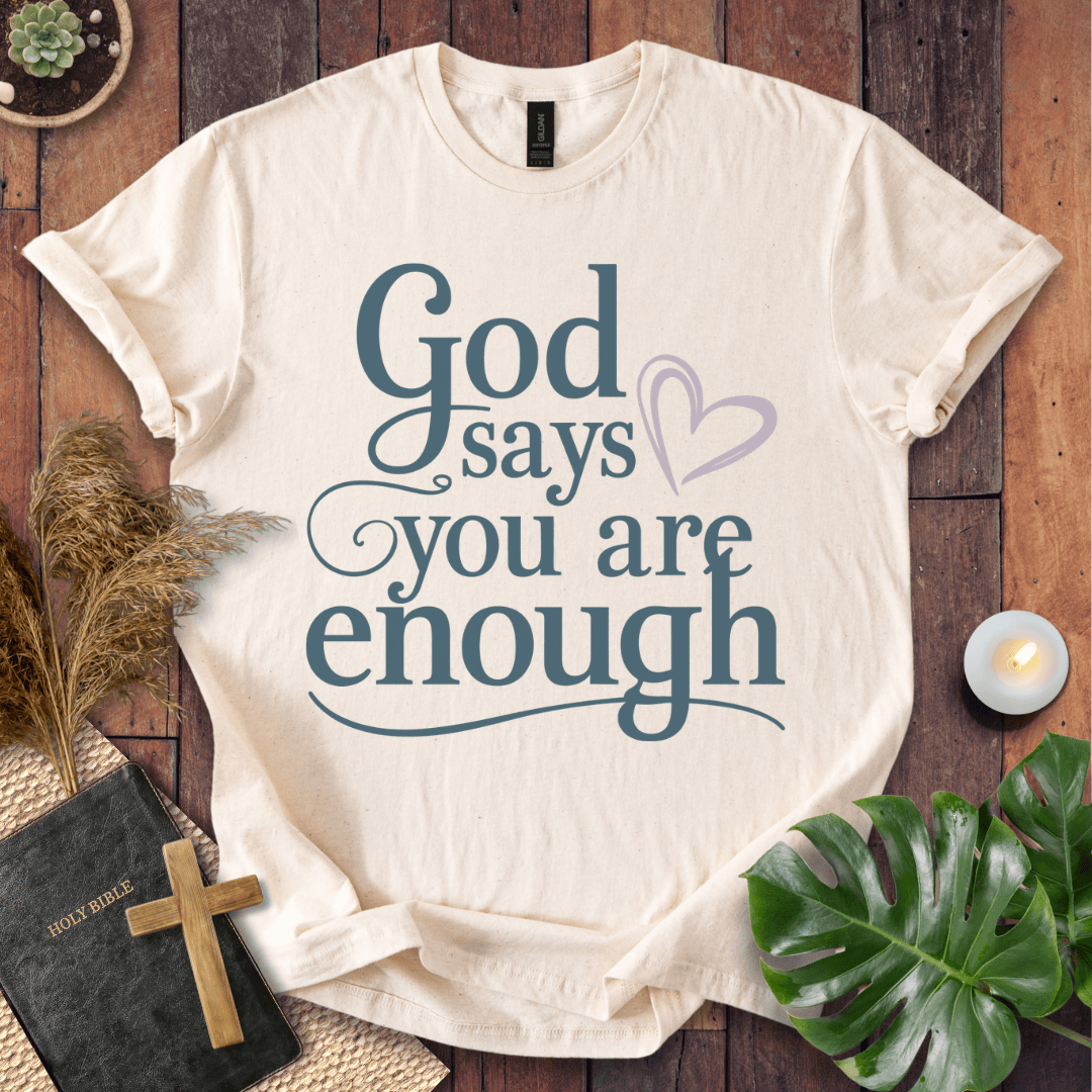 "God says you are enough" printed in teal on Christian t-shirt for women, styled with a Bible and wooden cross.