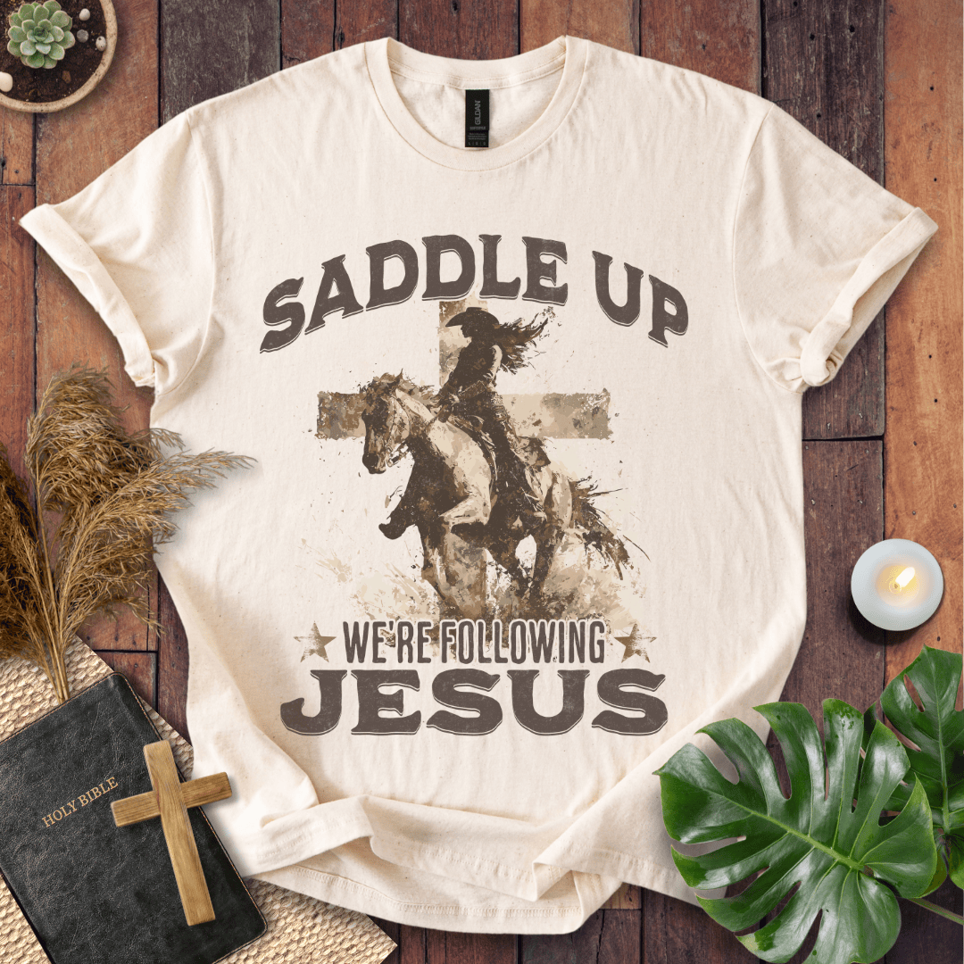 t-shirt featuring a cowgirl riding a horse in front of a cross with the text Saddle Up We're Following Jesus.