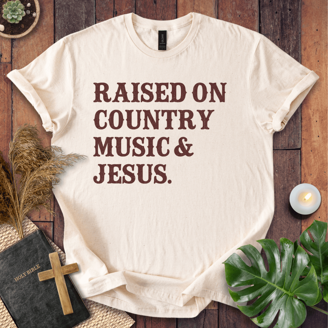 Christian t shirts for women with "Raised on Country Music & Jesus" in brown text on a rustic wood background.