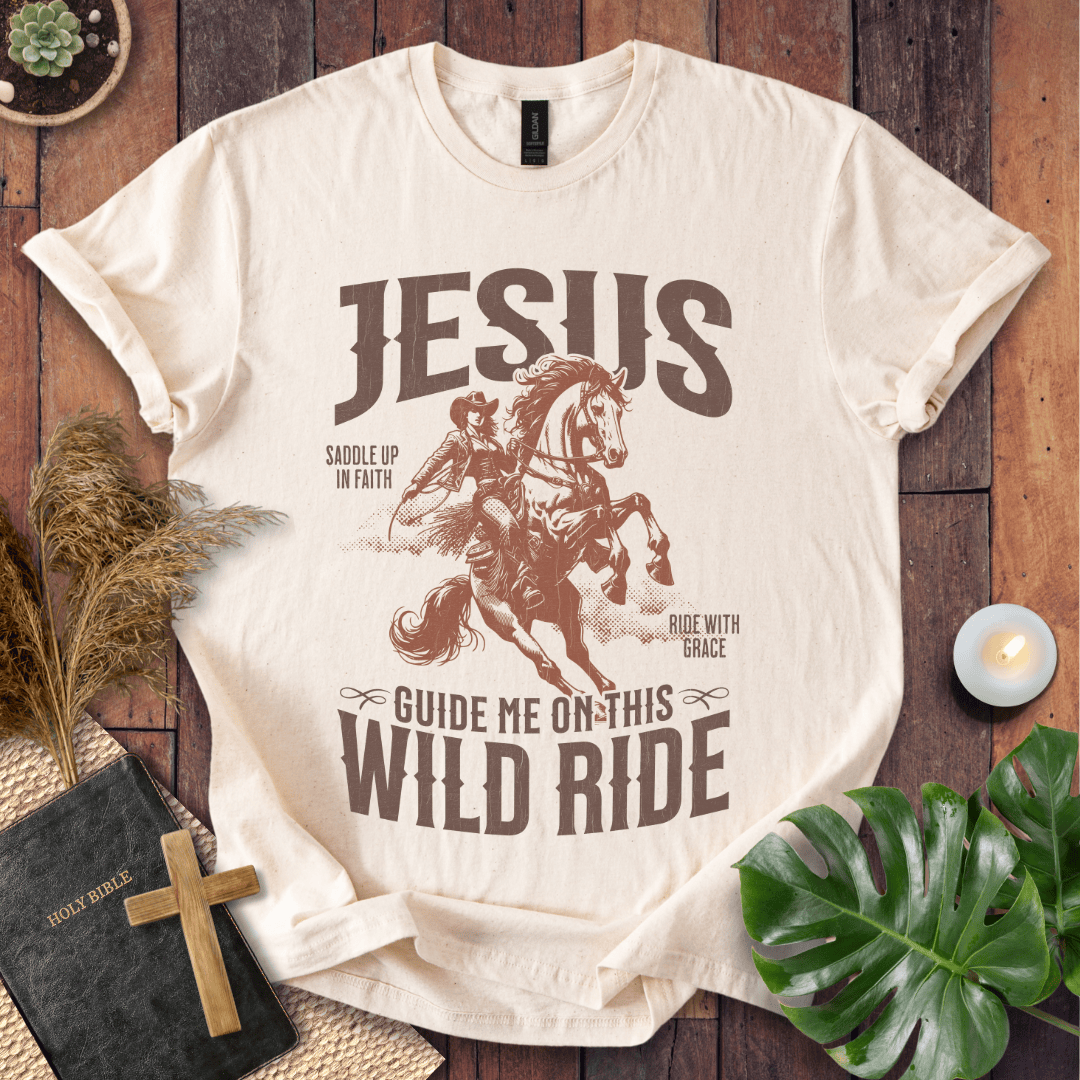 Beige t-shirt with graphic design of a person riding a horse and text on a wooden surface with decorative items.