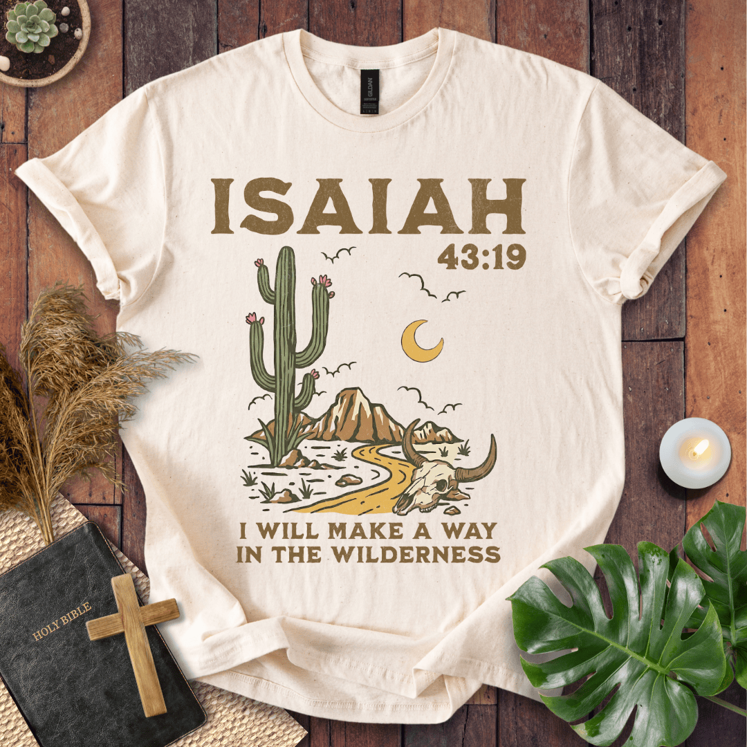 Beige t-shirt with cactus and skull design and 'ISAIAH 43:19' text on a wooden surface.