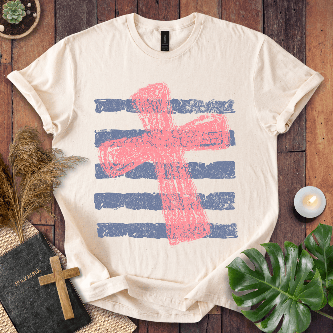 Distressed pink cross over blue horizontal stripes on a t-shirt, styled with a Bible and wooden cross.