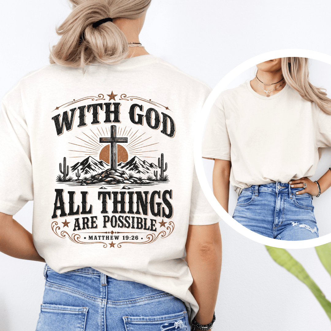A woman sitting on a bed wearing a western faith shirt featuring a desert cross design and Matthew 19:26 scripture.