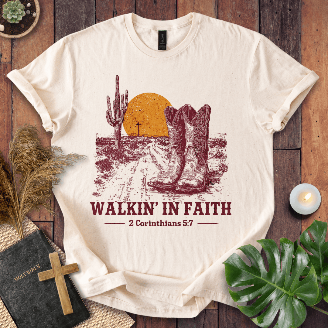 White t-shirt with cowboy boots and desert design, featuring 'Walkin' in Faith' text on a wooden surface.