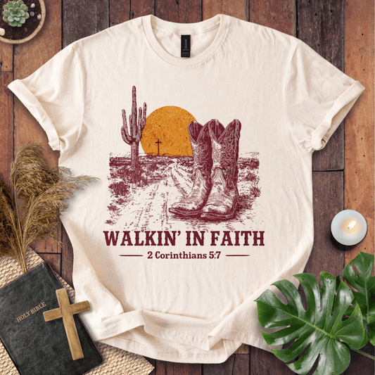 White t-shirt with cowboy boots and desert design, featuring 'Walkin' in Faith' text on a wooden surface.