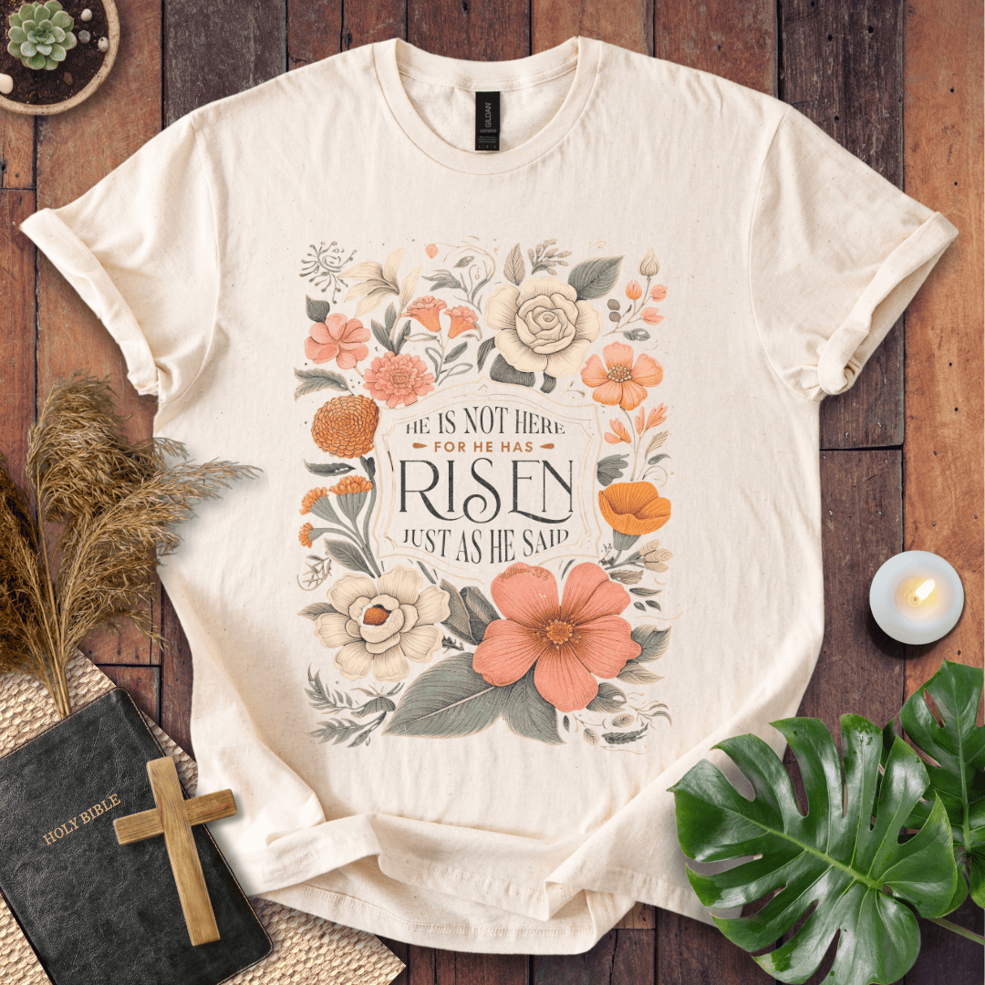 Christian Easter t-shirt with vintage flowers and He Is Risen Matthew 28:6 text on a rustic wood background.