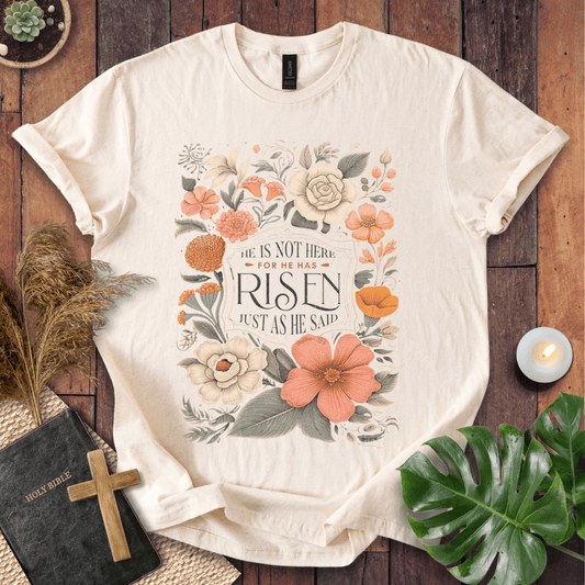 Christian Easter t-shirt with vintage flowers and He Is Risen Matthew 28:6 text on a rustic wood background.