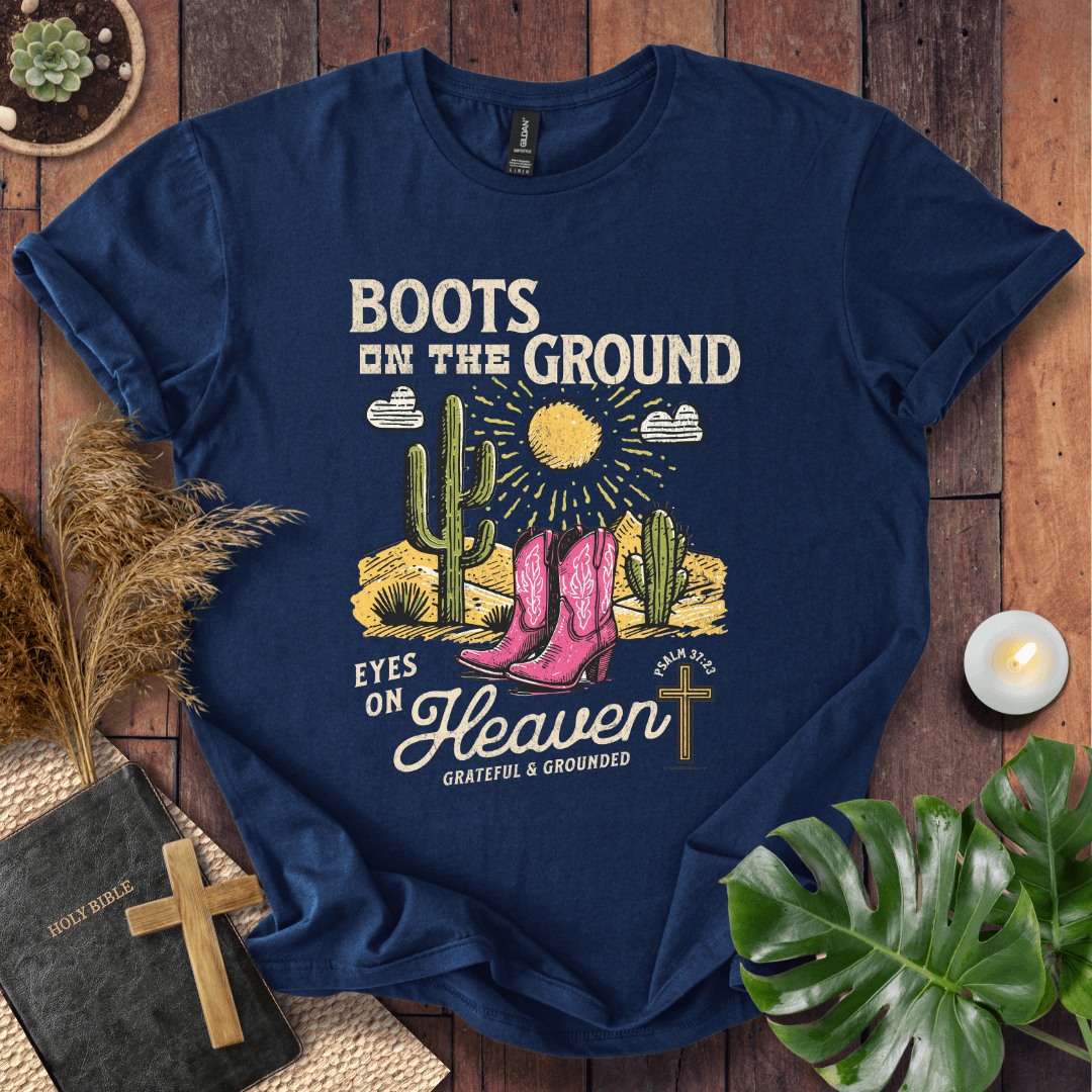 Christian t-shirt with pink cowboy boots, cacti, and "Boots on the Ground Eyes on Heaven" text for women's faith fashion.