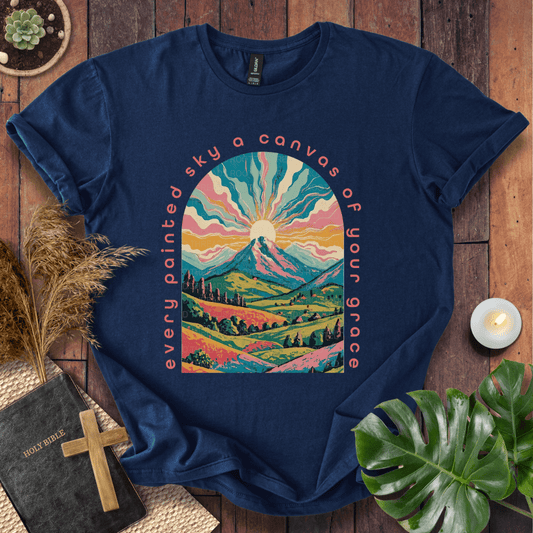 “Every painted sky a canvas of Your grace” Christian t-shirt—arched mountain sunrise with rays, rolling hills, floral accents.