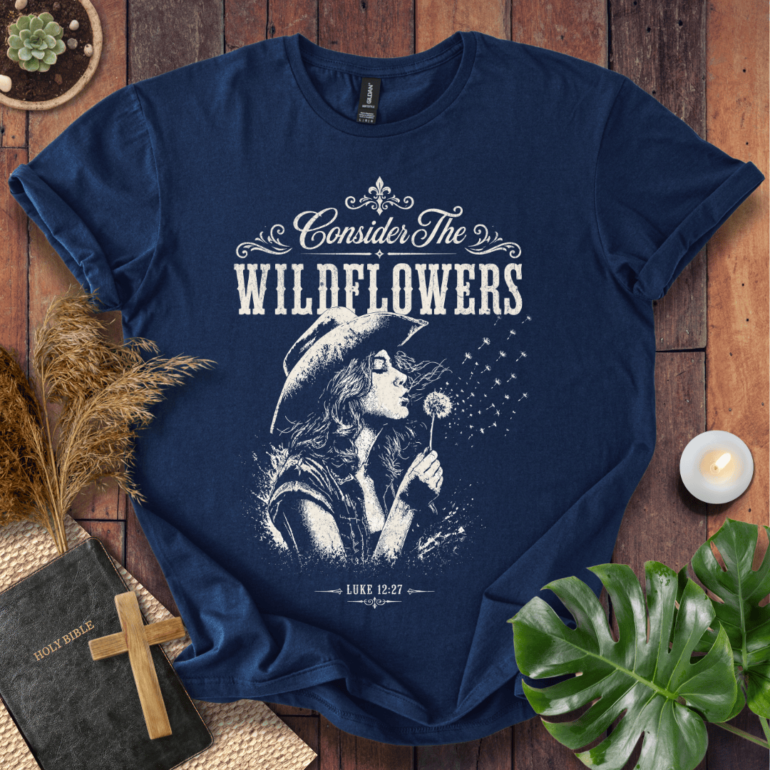 graphic tee reading Consider the Wildflowers Luke 12:27, featuring a woman in a cowboy hat blowing a dandelion.
