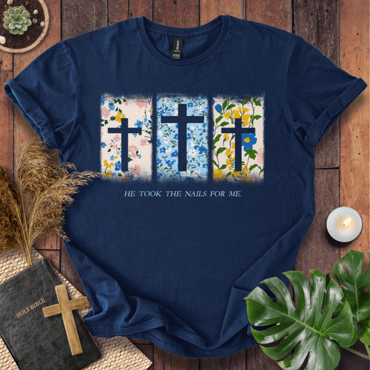 Christian Easter t-shirt with three floral crosses and "He Took The Nails For Me" text, styled on a rustic wood background.