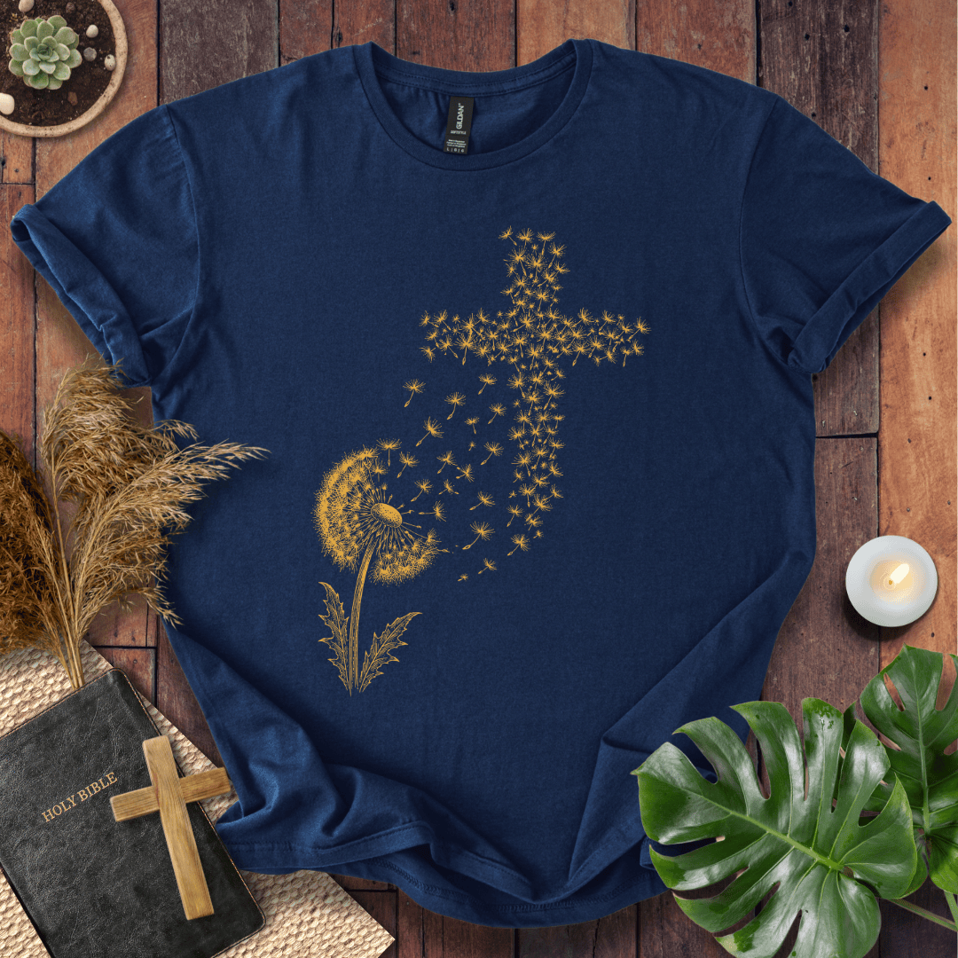 graphic t-shirt featuring a golden dandelion with seeds blowing in the wind to form a Christian cross shape.