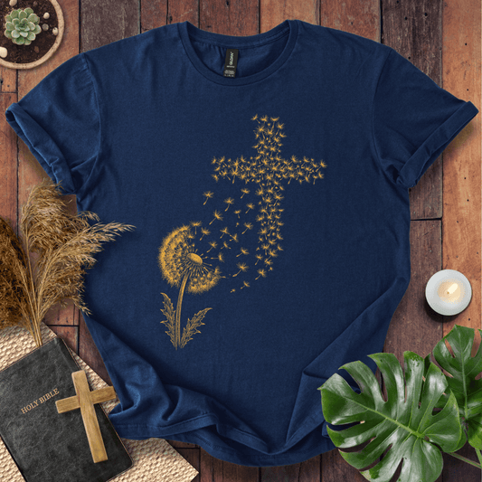graphic t-shirt featuring a golden dandelion with seeds blowing in the wind to form a Christian cross shape.