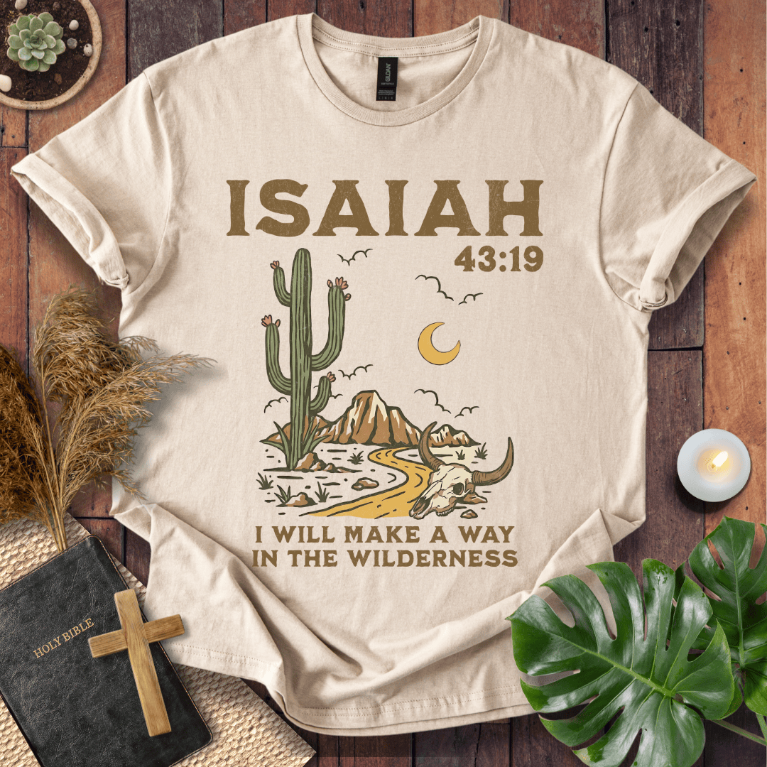Beige t-shirt with cactus and mountain design and 'ISAIAH 43:19' text on a wooden surface.