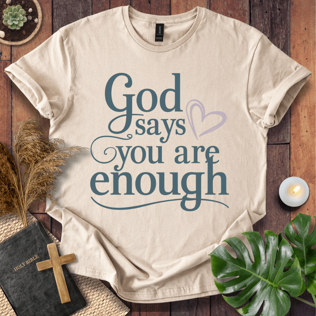 "God says you are enough" printed in teal on Christian t-shirt for women, styled with a Bible and wooden cross.