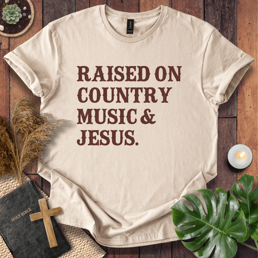 Christian t shirts for women with "Raised on Country Music & Jesus" in brown text on a rustic wood background.