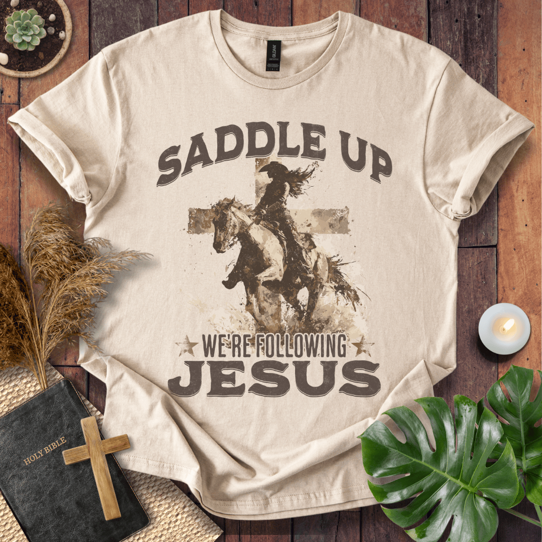 t-shirt featuring a cowgirl riding a horse in front of a cross with the text Saddle Up We're Following Jesus.