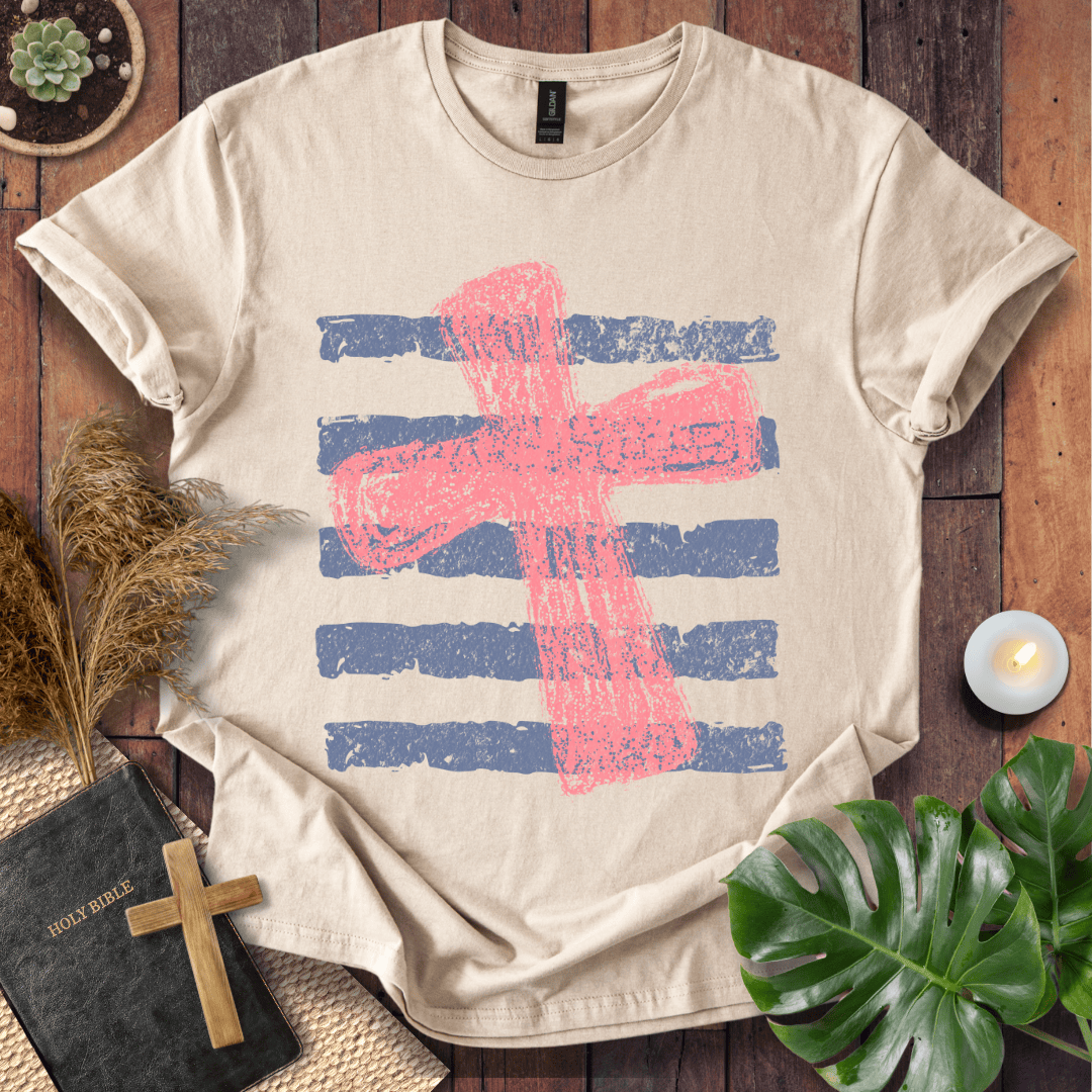 Distressed pink cross over blue horizontal stripes on a t-shirt, styled with a Bible and wooden cross.