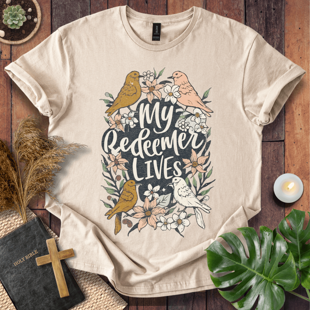 Christian Easter t-shirt with My Redeemer Lives text and birds on a wooden table next to a Holy Bible and a wooden cross.