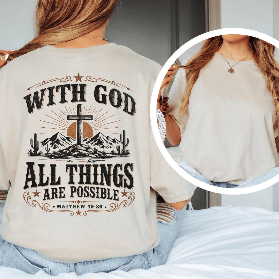 A woman sitting on a bed wearing a western faith shirt featuring a desert cross design and Matthew 19:26 scripture.