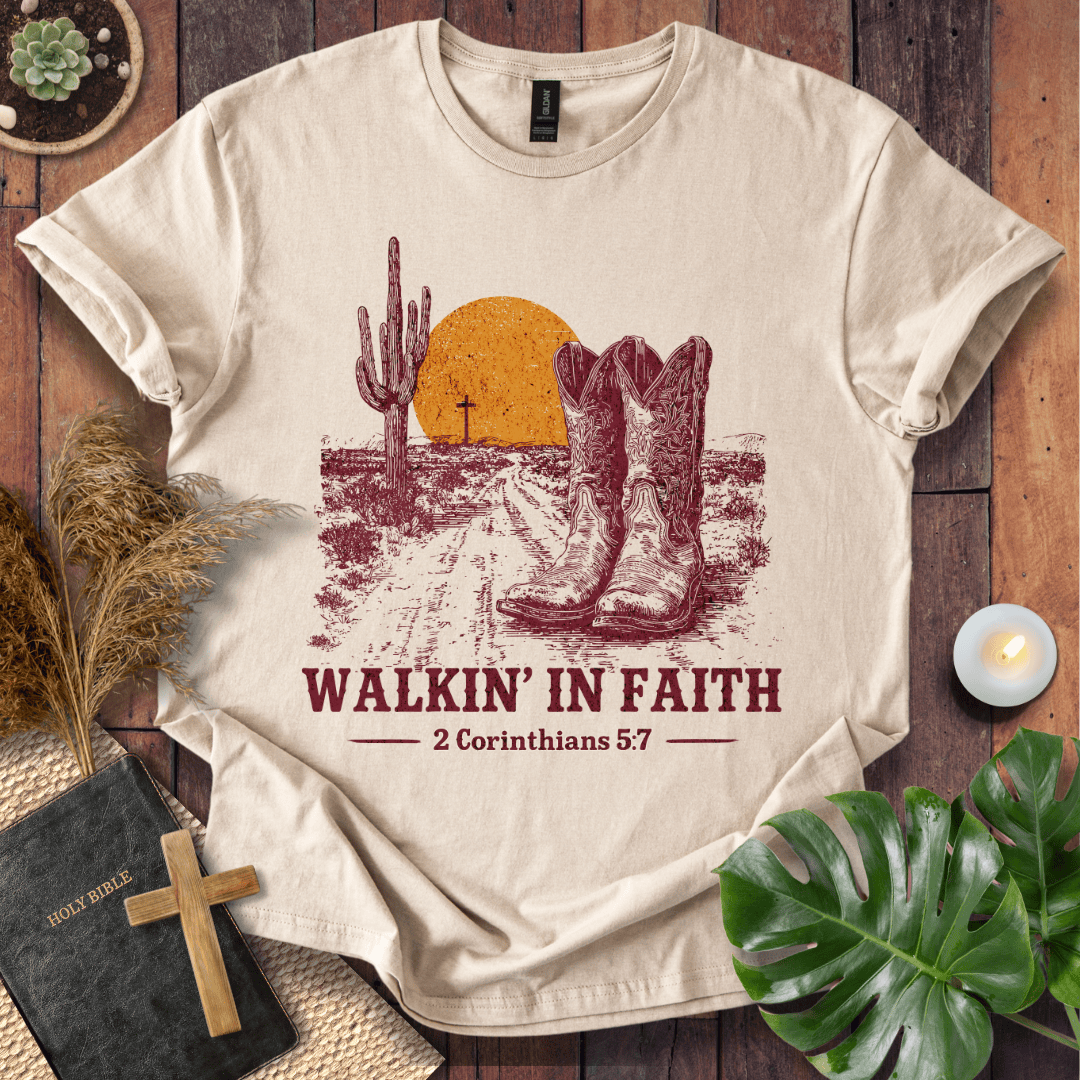 Beige t-shirt with cowboy boots and desert graphic on a wooden surface with plants and a Bible.