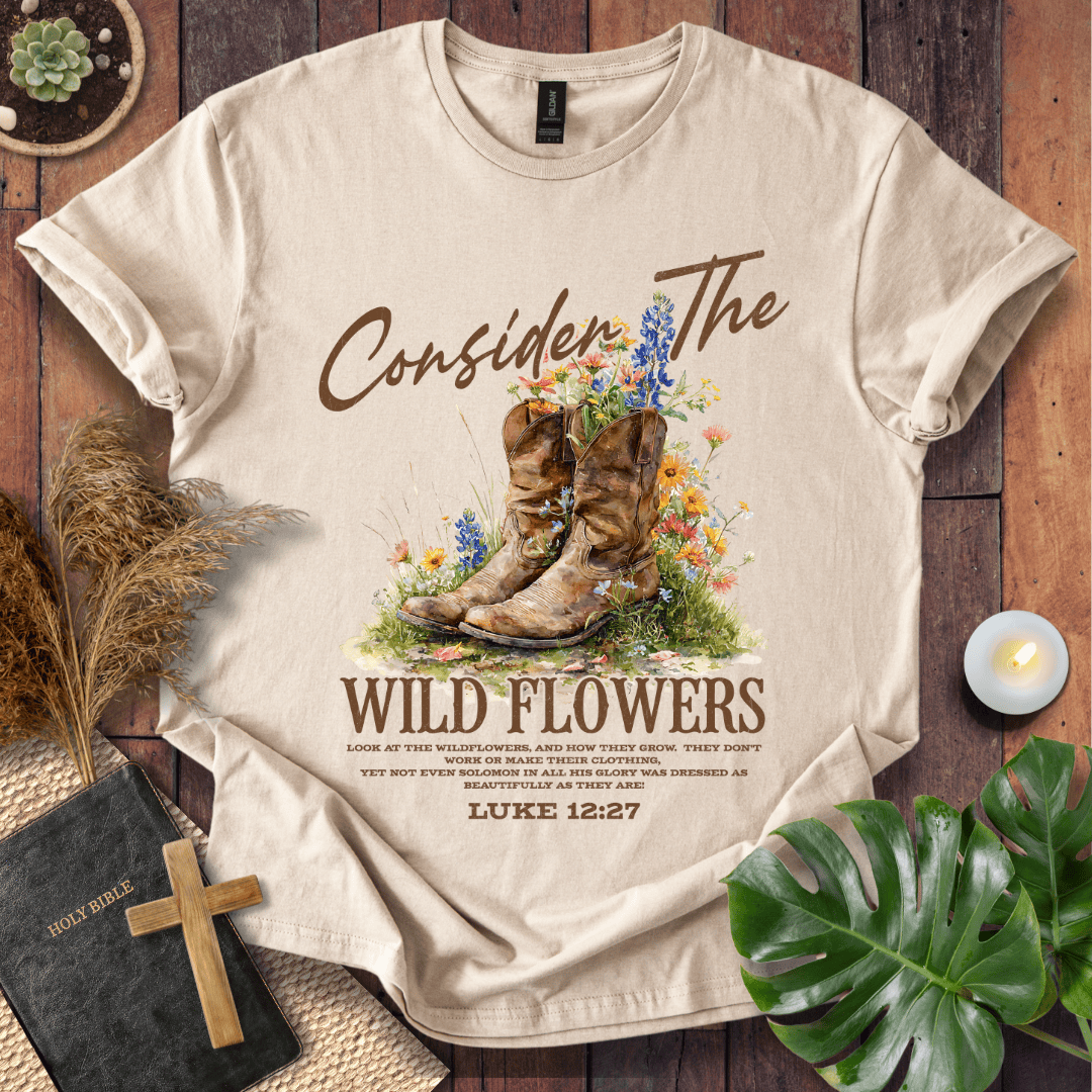 Western wildflower graphic tee with bible verse shirts text showing Luke 12:27 and boots on a natural cream shirt.