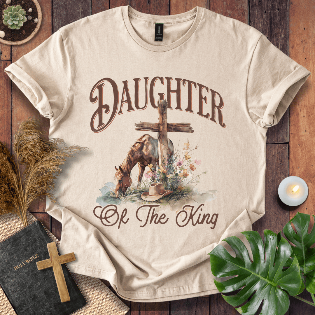 t-shirt with "Daughter of the King" text, a grazing horse, wooden cross, cowboy hat, and wildflowers.