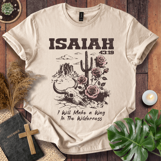 Beige t-shirt with skull, cactus, and roses design on a wooden surface with plants and a Bible.