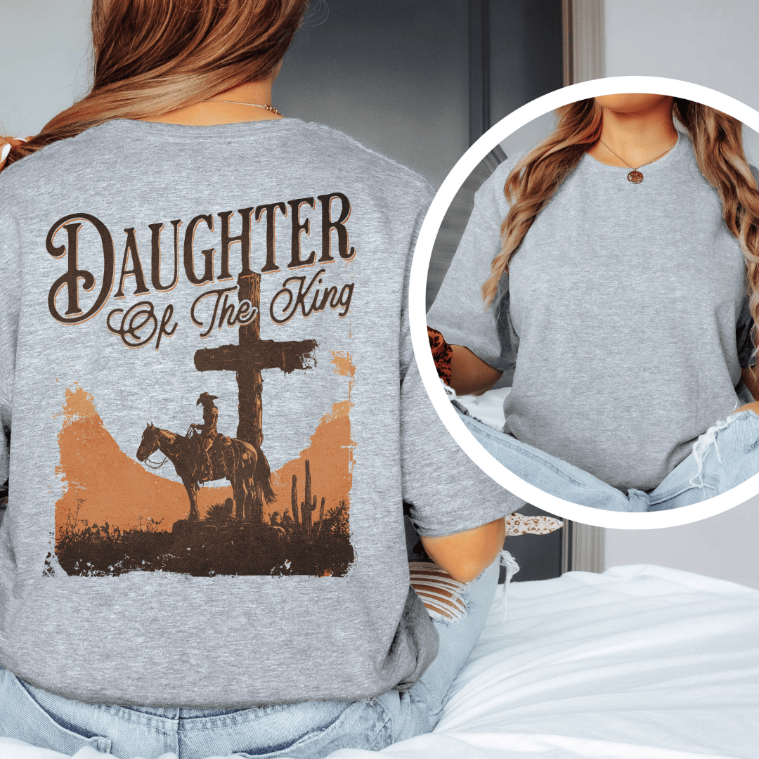 A woman wearing a graphic t-shirt with a western desert cross, cowboy on a horse, and Daughter of the King text.