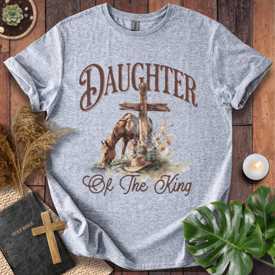 t-shirt with "Daughter of the King" text, a grazing horse, wooden cross, cowboy hat, and wildflowers.