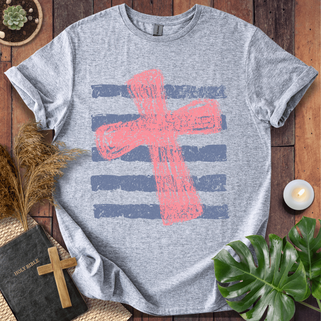 Distressed pink cross over blue horizontal stripes on a t-shirt, styled with a Bible and wooden cross.