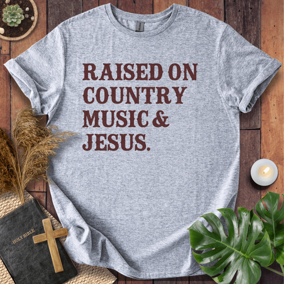 Christian t shirts for women with "Raised on Country Music & Jesus" in brown text on a rustic wood background.