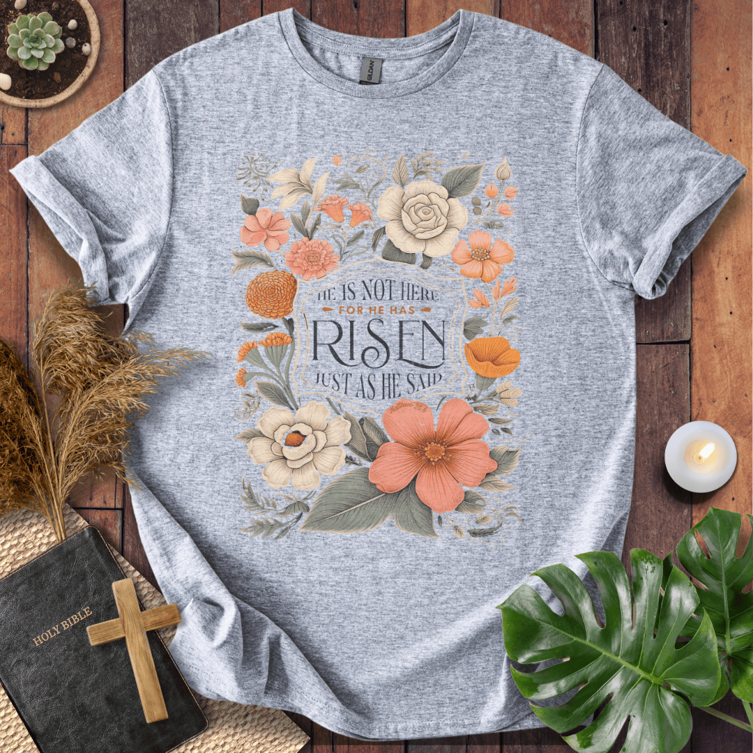 Christian Easter t-shirt with vintage flowers and He Is Risen Matthew 28:6 text on a rustic wood background.