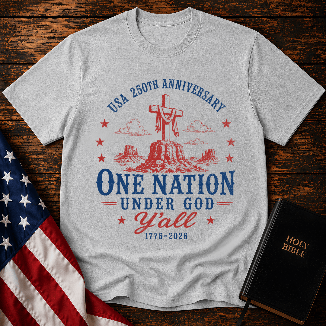 Patriotic western graphic tee featuring a wooden cross on a desert mesa with text One Nation Under God Y'all 1776-2026.