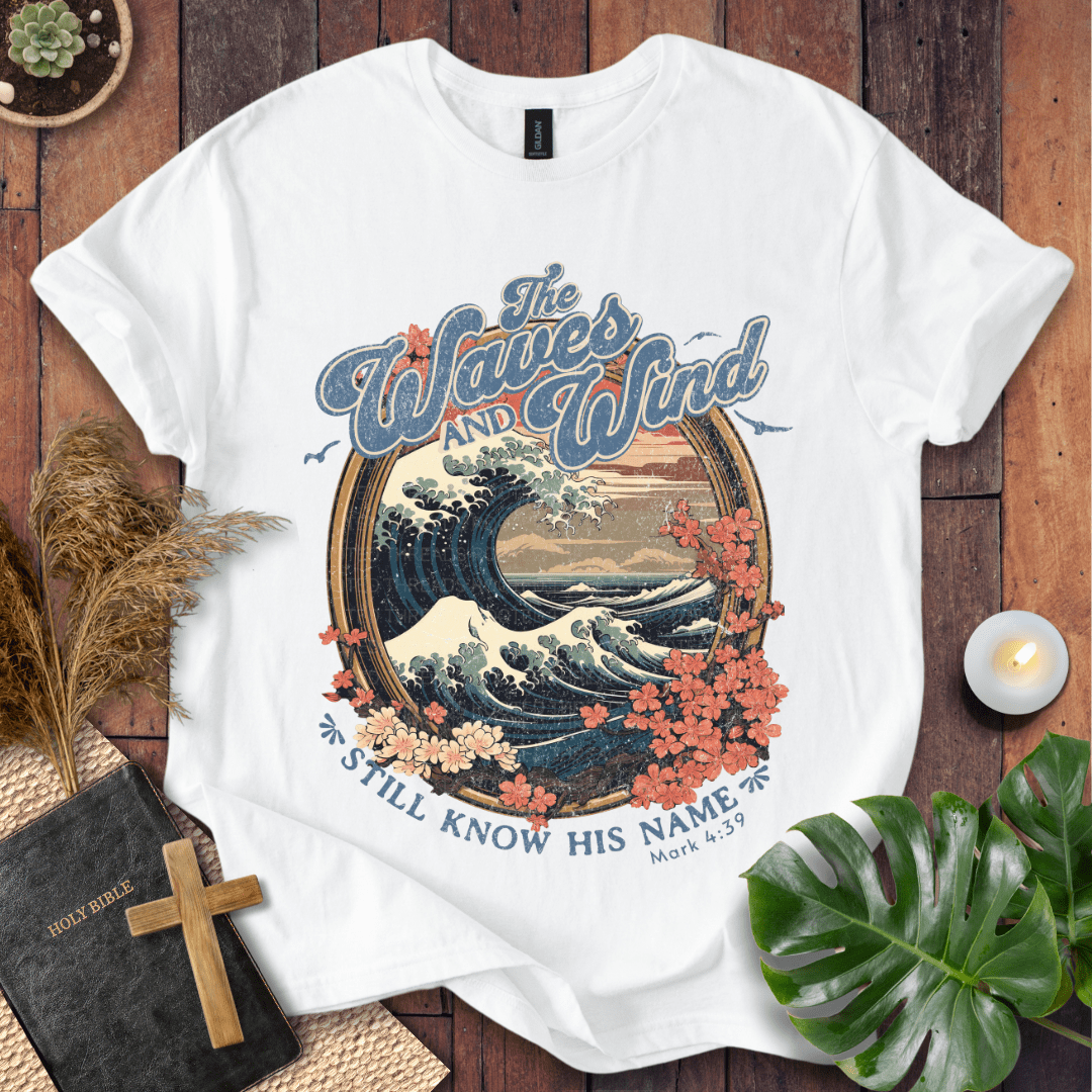 The Waves and Wind Still Know His Name Christian t-shirt in sand—vintage wave, sunset, and floral frame, Mark 4:39.