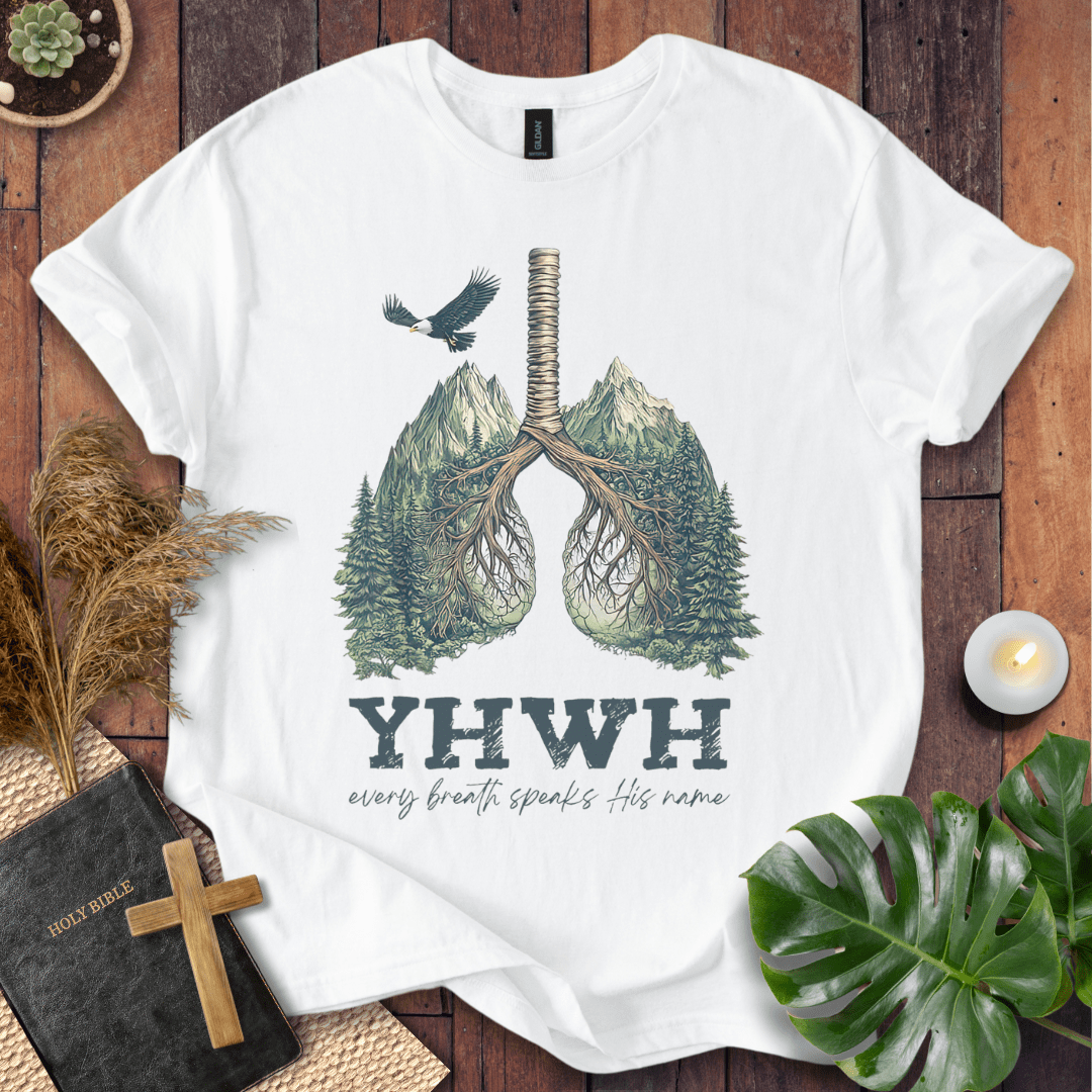 Christian t-shirt with YHWH design, tree-lung illustration, mountains, and “Every Breath Speaks His Name” text, laid flat with Bible and plants.