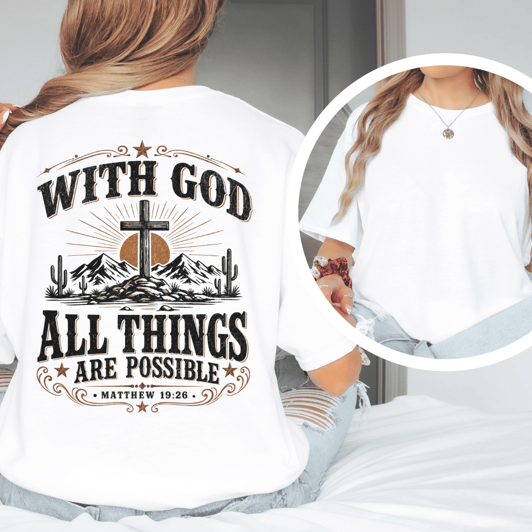 A woman sitting on a bed wearing a western faith shirt featuring a desert cross design and Matthew 19:26 scripture.