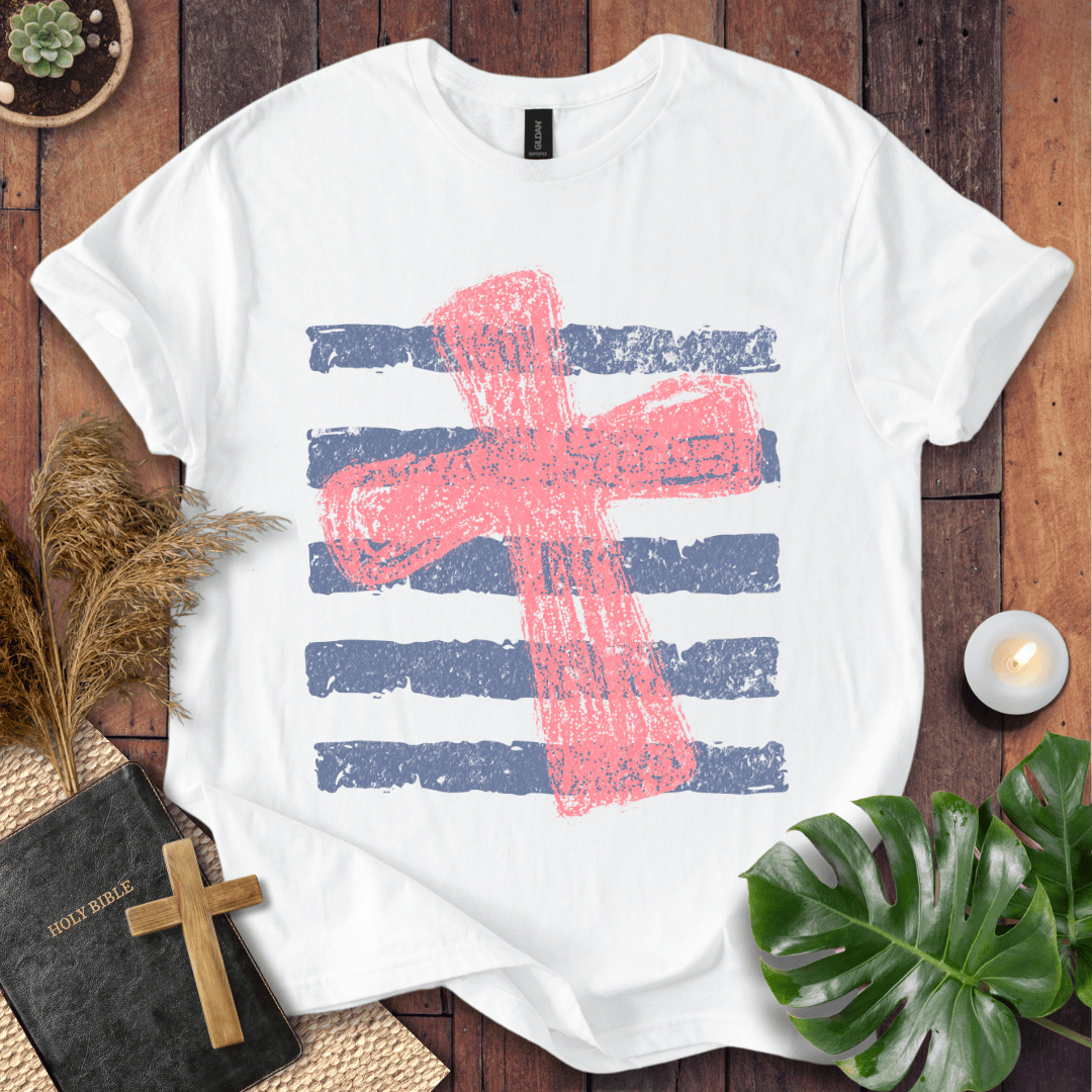 Distressed pink cross over blue horizontal stripes on a t-shirt, styled with a Bible and wooden cross.
