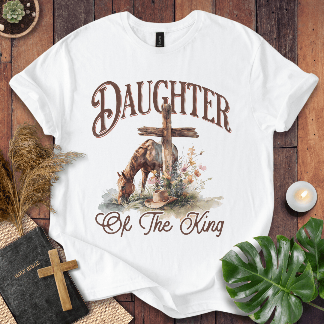 t-shirt with "Daughter of the King" text, a grazing horse, wooden cross, cowboy hat, and wildflowers.