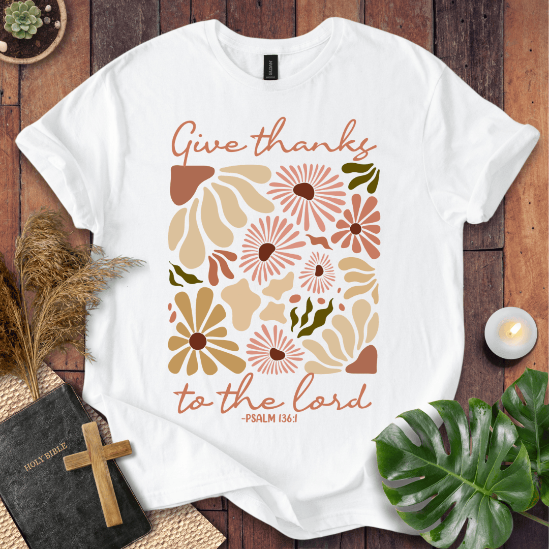Give Thanks to the Lord Psalm 136:1 white graphic t-shirt with retro boho rust and sage wildflowers on a wood background.