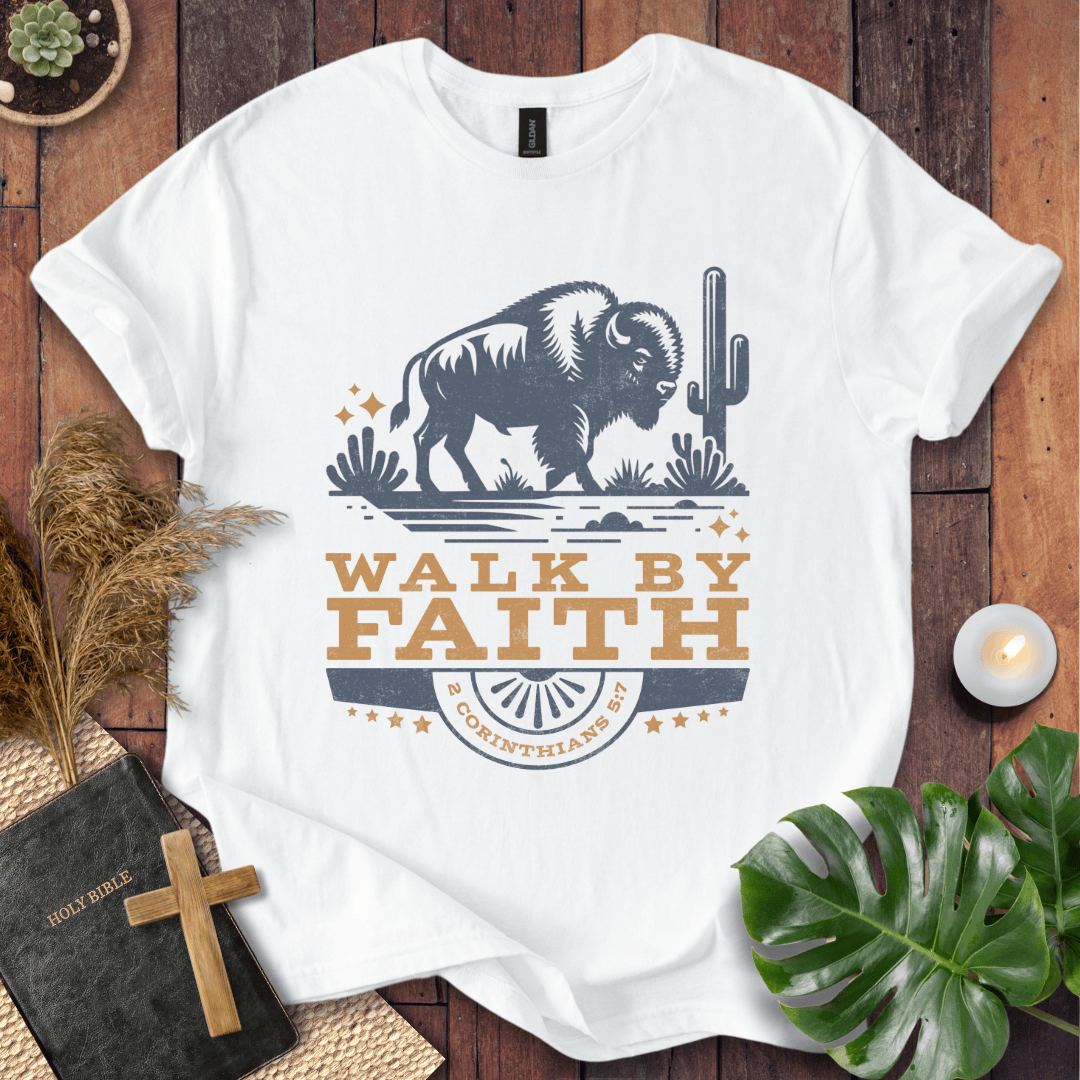 White t-shirt with a bison graphic and 'Walk by Faith' text on a wooden surface with plants and a Bible.